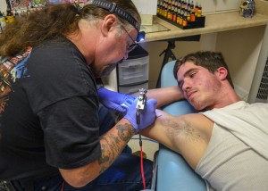 Megan Godby//Contributing photographer / Stash tattoos the word "Brotherhood" on customer, Gregory Jones' bicep.