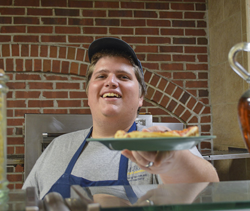 Hannah Fowl/The News Tyler James, senior, Palmdale, Calif., serves a personal pan pizza to a student as part of his many duties as a student worker at Winslow Dining Hall. 